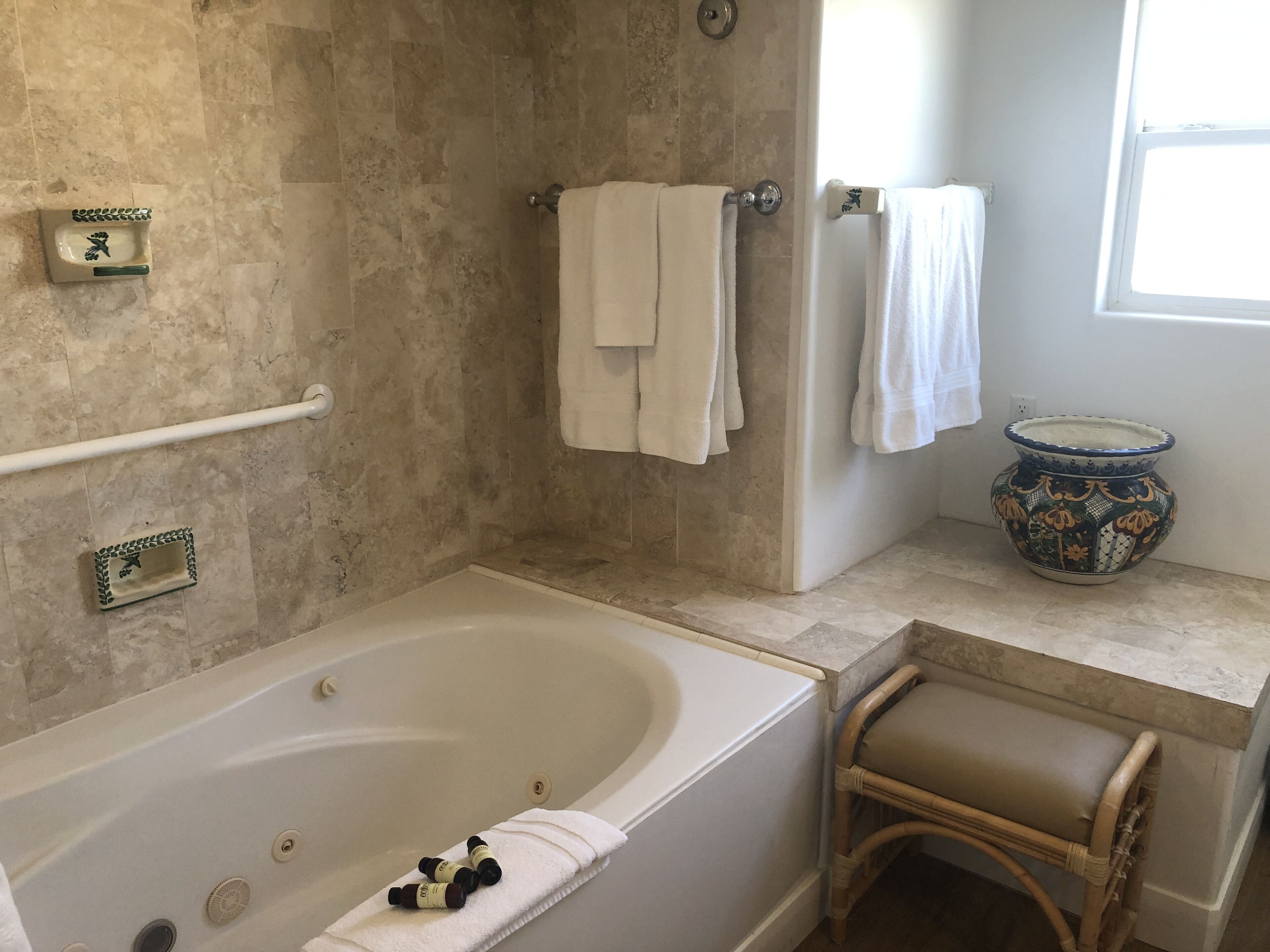 A bathroom with a bathtub, a shower, a toilet, and a sink. There are towels hanging on the wall and a decorative vase on the counter.