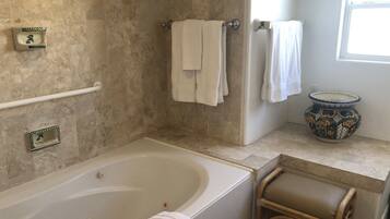 A bathroom with a bathtub, a shower, a toilet, and a sink. There are towels hanging on the wall and a decorative vase on the counter.
