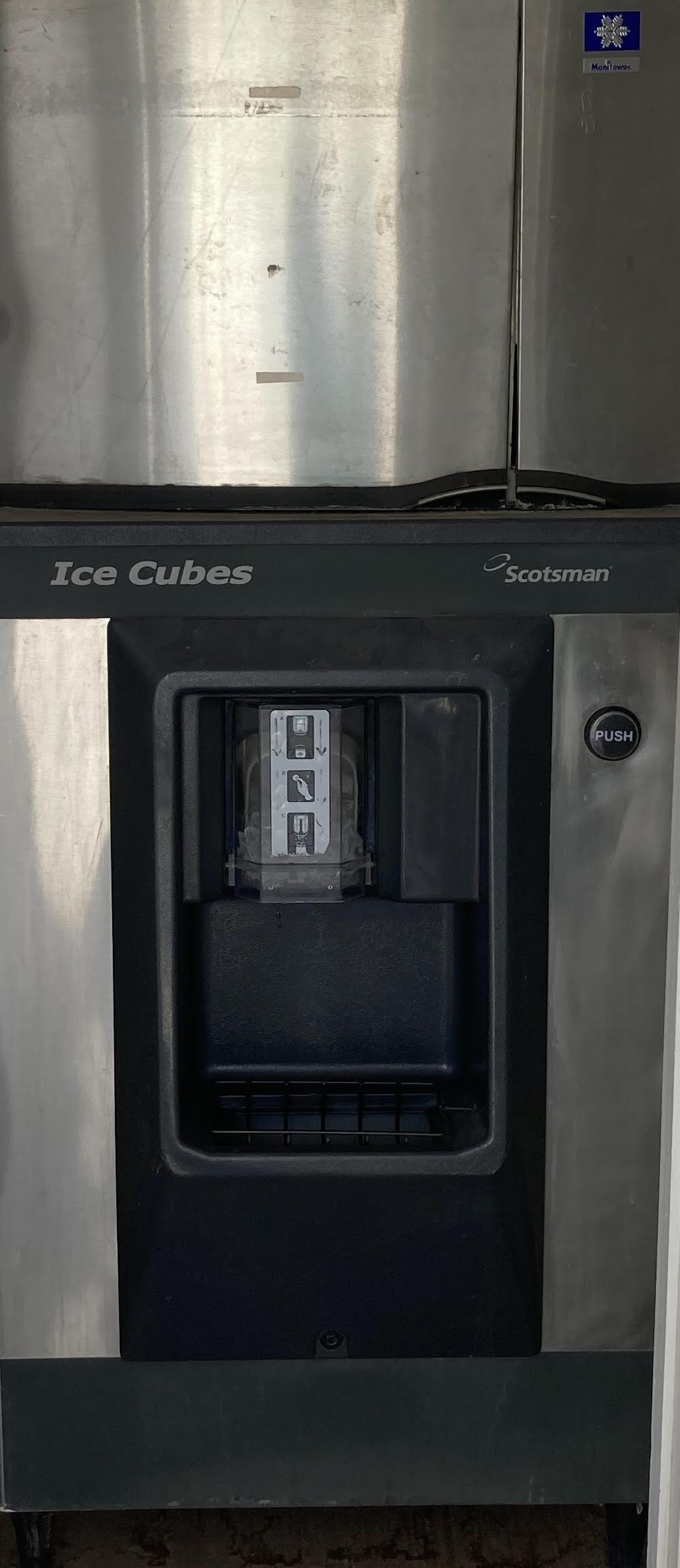 A stainless steel ice cube dispenser with a push button, labeled "Ice Cubes" and "Scotsman."