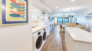 A modern kitchen with a built-in washer and dryer, wooden cabinets, and a dining area with a view of the ocean. - OCEAN'S REACH 4C2: 2nd Floor, Beautiful Gulf Views w/Easy Beach Access! (Sanibel Island)