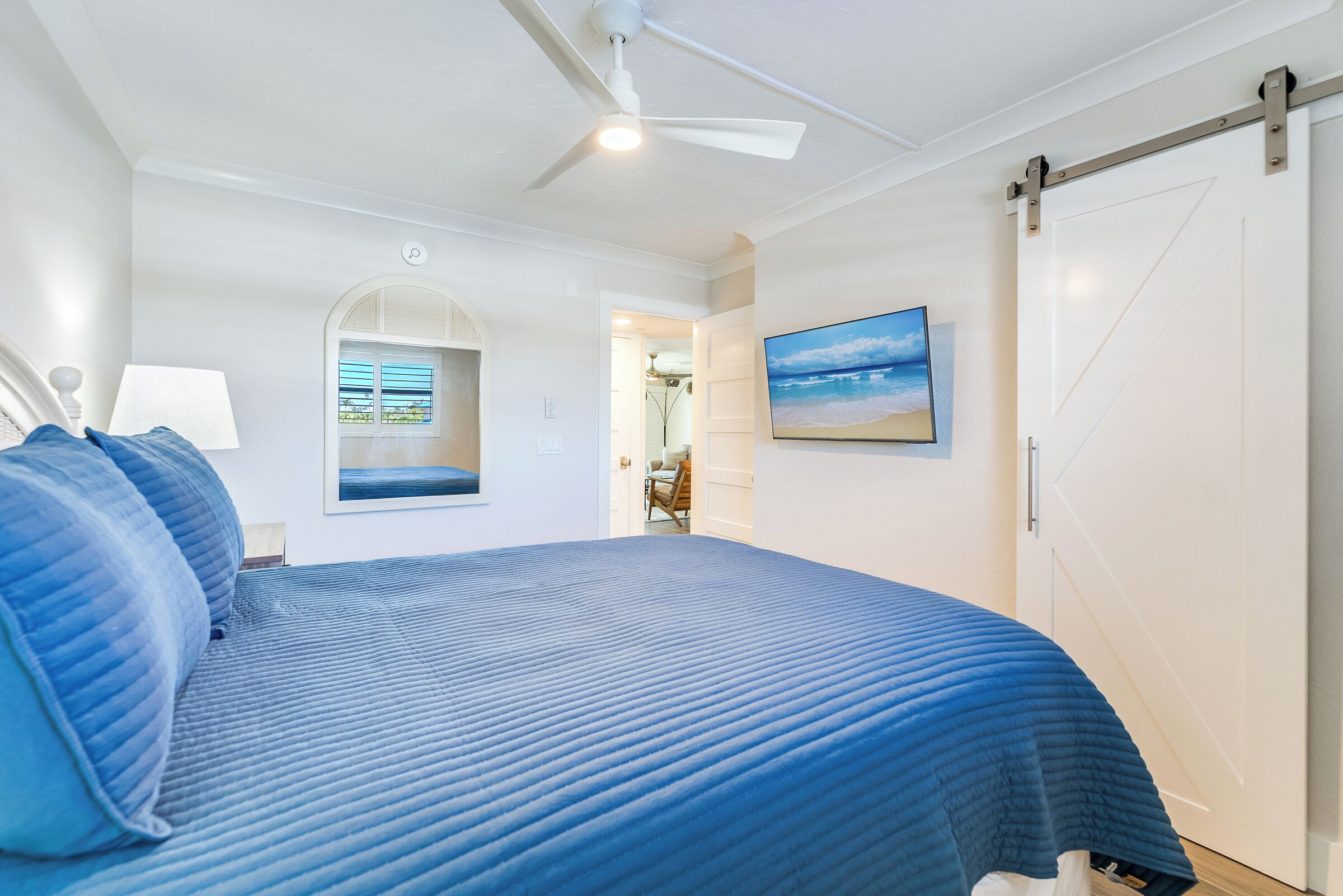 A bedroom with a large bed, a ceiling fan, a sliding door, and a framed picture on the wall.
