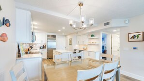A modern kitchen with white cabinets, a dining table with chairs, and a chandelier. - OCEAN'S REACH 4C2: 2nd Floor, Beautiful Gulf Views w/Easy Beach Access! (Sanibel Island)