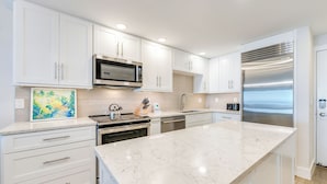 A modern kitchen with white cabinetry, a large island, stainless steel appliances, and a painting on the wall. - OCEAN'S REACH 4C2: 2nd Floor, Beautiful Gulf Views w/Easy Beach Access! (Sanibel Island)