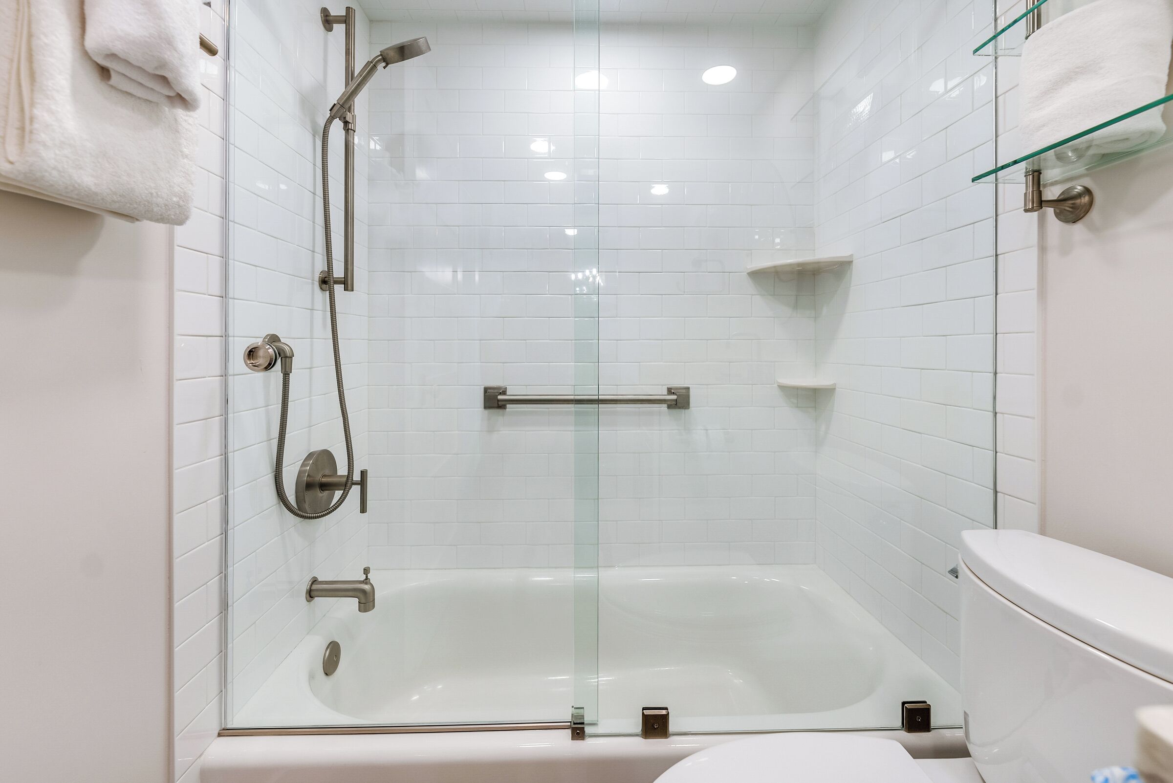 A modern bathroom with a glass-enclosed shower, a white bathtub, and a toilet.