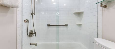 A modern bathroom with a glass-enclosed shower, a white bathtub, and a toilet.