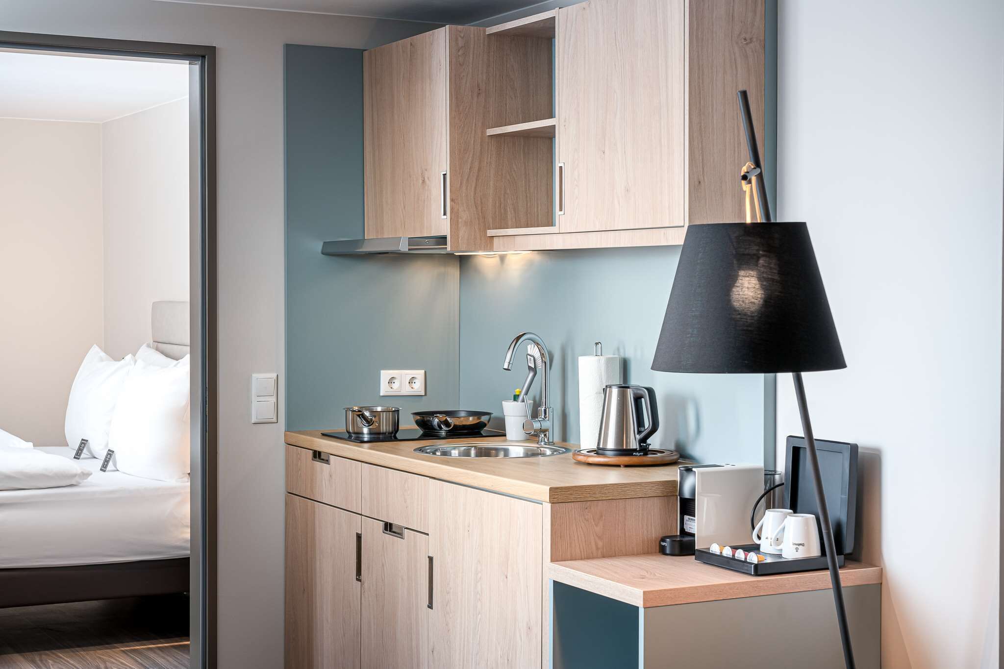 A compact kitchen with wooden cabinets, a sink, a kettle, and a coffee maker.