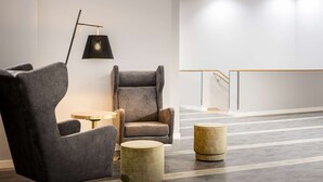 A modern hotel lobby with a grey armchair, a round table, and a lamp. - elaya hotel oberhausen, Trademark by Wyndham (Oberhausen)
