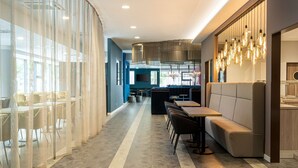 A modern restaurant with a long counter, seating area, and a kitchen visible in the background. - elaya hotel oberhausen, Trademark by Wyndham (Oberhausen)