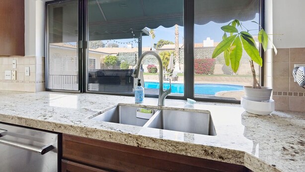 A kitchen with a double sink, a countertop, and a view of a swimming pool through large sliding glass doors. - Centrally located Palm Desert Oasis (Palm Desert)