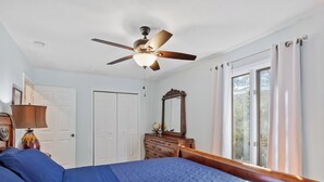 A bedroom with a bed, a ceiling fan, a dresser, a mirror, and a window with curtains.