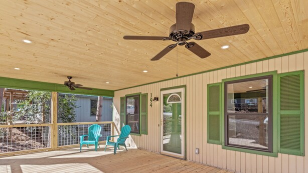 A covered porch with a ceiling fan, wooden deck, and green shutters.