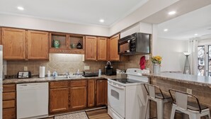 A modern kitchen with wooden cabinets, a white dishwasher, a stove, and a microwave.