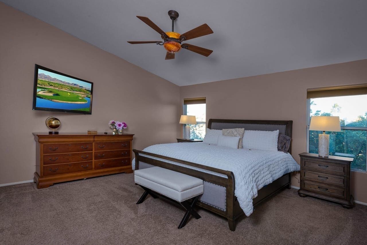 A bedroom with a bed, a dresser, a bench, a ceiling fan, a TV, and two bedside lamps.