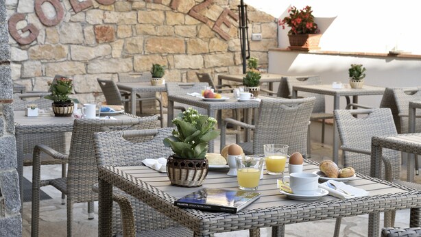 An outdoor café with wicker furniture, stone walls, and potted plants. - Hotel Goloritzé (Baunei)