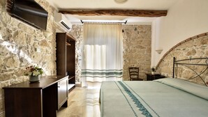 A bedroom with stone walls, a wooden bed frame, a nightstand, and a desk with a vase of flowers. - Hotel Goloritzé (Baunei)