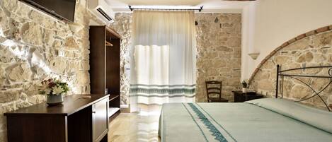 Un dormitorio con paredes de piedra, un cabecero de madera, una mesita de noche y un escritorio con un florero.