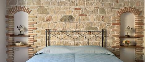 Un dormitorio con pared de piedra, cabecero de metal y cama con colcha azul estampada.