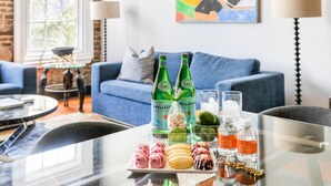 Una sala de estar moderna con un sofá azul, una mesa de centro de vidrio y un recipiente decorativo. Hay dos botellas de agua Pellegrino y dos botellas de agua Luxurious sobre la mesa.
