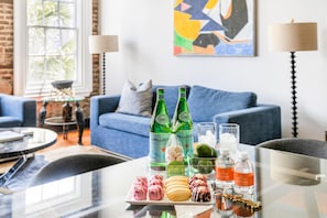 Un salon moderne avec un canapé bleu, une table basse en verre et un bol décoratif. On peut voir deux bouteilles d’eau Pellegrino et deux bouteilles d’eau de la marque Luxurious sur la table.