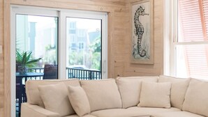 A beige sectional sofa in a room with wooden paneling, large windows, and a seahorse painting on the wall. - Hammock Dunes I - Private Cottage Beach Side (Orange Beach)