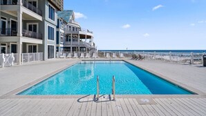A swimming pool with a wooden deck, a white fence, and a building with balconies and a covered area. - Hammock Dunes I - Private Cottage Beach Side (Orange Beach)