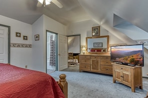 Een slaapkamer met een bed, een dressoir, een televisie en een deur naar een andere kamer.