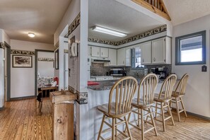 Een keuken met witte kasten, een granieten aanrechtblad en een vast eiland met houten stoelen.