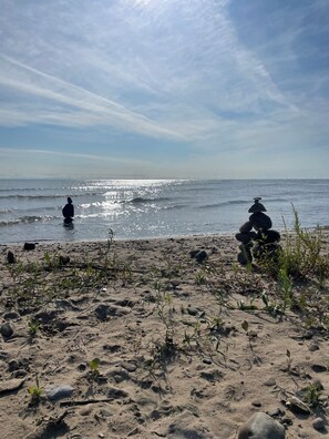 A beach with a stack of stones and a person sitting on the sand.