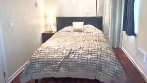 A neatly made bed with a patterned bedspread, a bedside lamp, and a nightstand. - Bamboo House Studio - Clean and Cozy Apartment ready just for you! (Eugene)