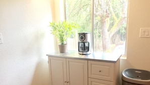 A kitchen with white cabinets, a coffee maker, and a trash can. - Bamboo House Studio - Clean and Cozy Apartment ready just for you! (Eugene)