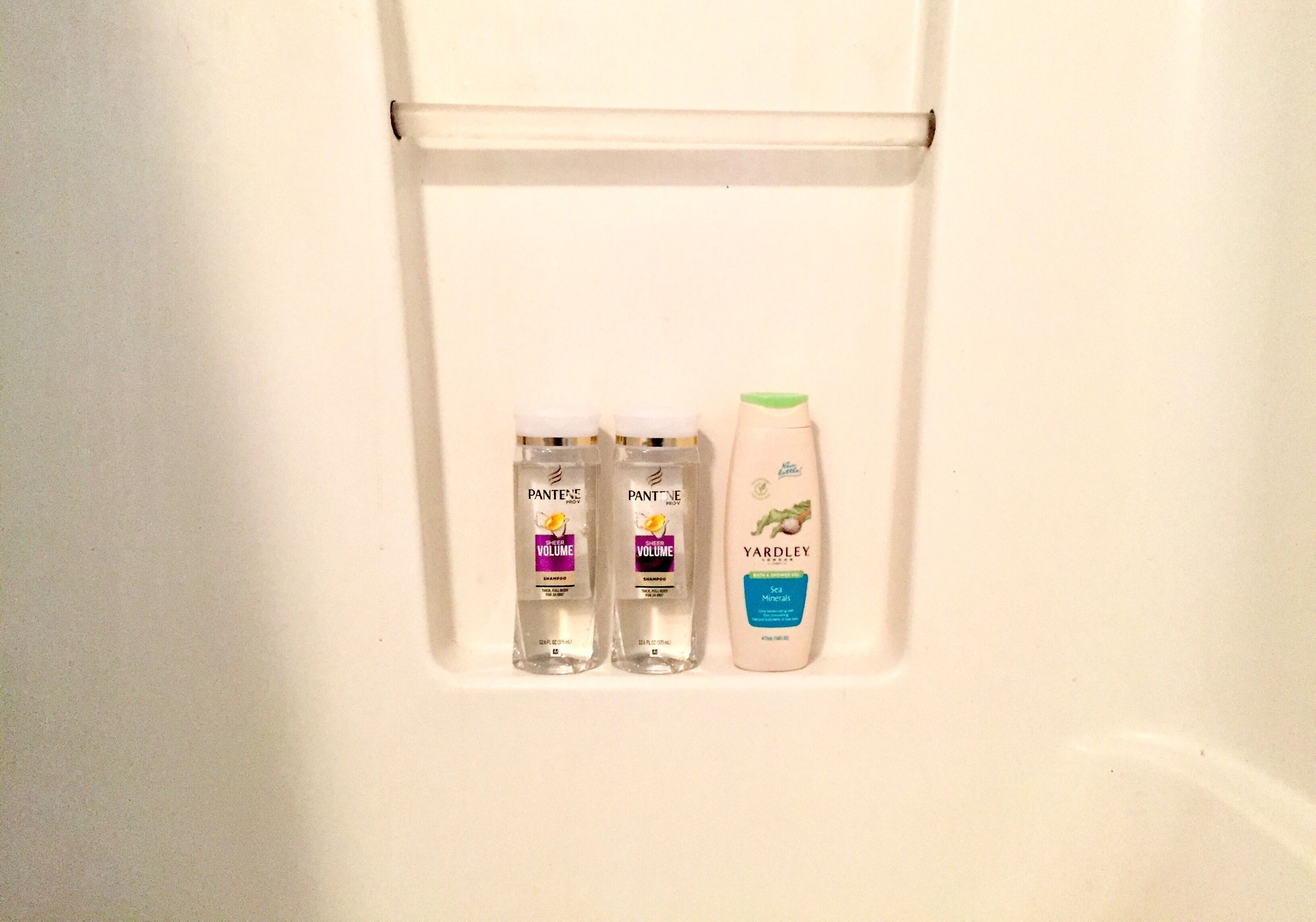 Uno scaffale bianco con tre bottiglie di shampoo Pantene Volume e una bottiglia di lozione Yardley Sea Minerals.