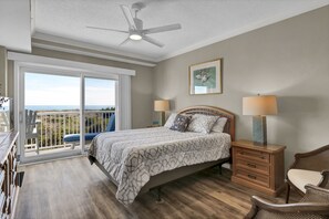 A bedroom with a bed, bedside tables, a chair, a ceiling fan, and a view of the outdoors.