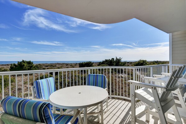 A deck with white railings, blue-striped cushions, and a white table.