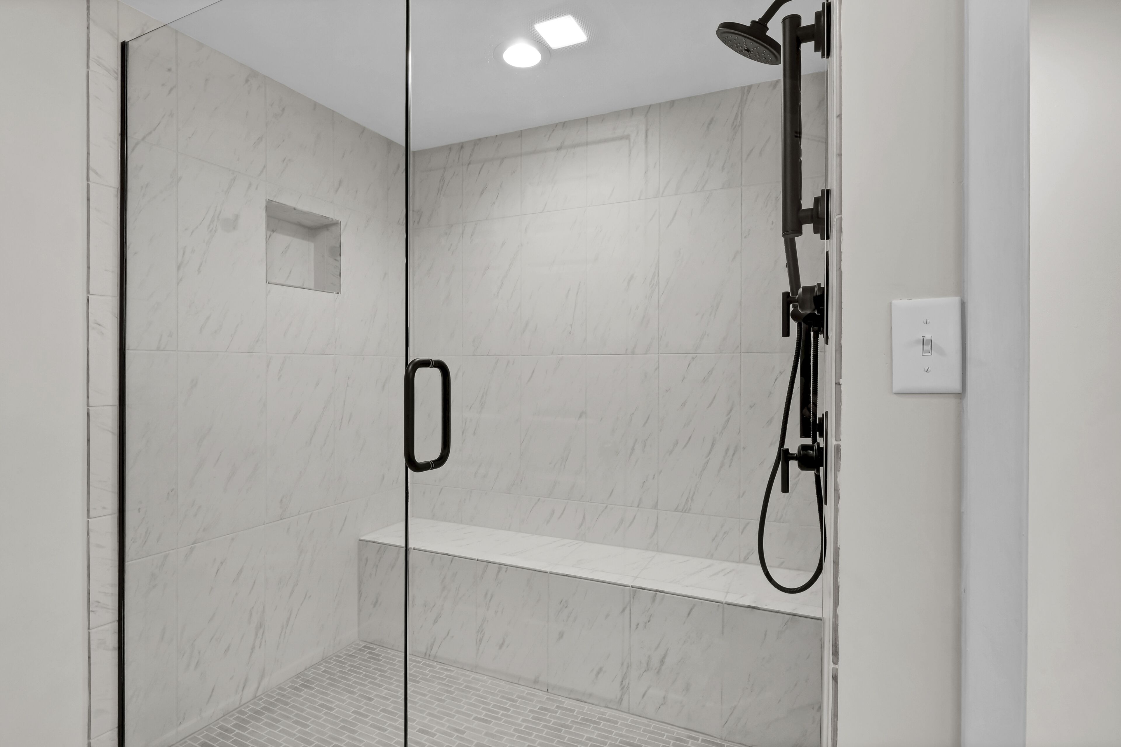 A modern shower area with glass doors, a built-in shelf, and a handheld showerhead.