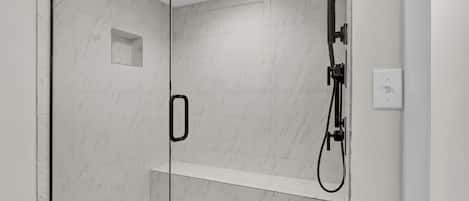 A modern shower area with glass doors, a built-in shelf, and a handheld showerhead.