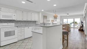 Una cocina moderna con armarios blancos, una isla central y un comedor con vistas.