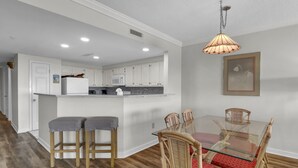 Una cocina moderna con armarios blancos, una isla de cristal y un comedor con sillas de mimbre y una mesa de cristal.