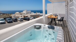 Un balcón con jacuzzi, una mesa con sillas y vistas al mar y edificios.