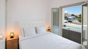 Un dormitorio con una cama grande, una mesita de noche con lámpara y vistas a una piscina y coches afuera.