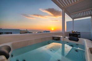 Un jacuzzi en la azotea con vistas al atardecer, una mesa con dos copas de vino y una planta pequeña.