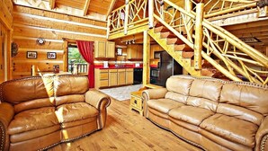 A log cabin interior with a wooden staircase, leather sofas, a kitchen area, and a dining table. - Passion's Peak - Sleeps 2 (Sevierville)