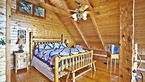A wooden cabin bedroom with a wooden bed, a nightstand, a lamp, a ceiling fan, and a window. - Passion's Peak - Sleeps 2 (Sevierville)