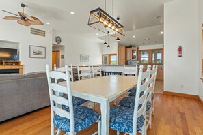 A dining area with a wooden table and white chairs with blue patterned cushions, a ceiling fan, and recessed lighting. - Gramp's Dream: 440 Ft to Beach, Pool, Hot Tub & Dog-friendly (Southern Shores)