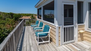 Eine Holzterrasse mit vier Stühlen und einem überdachten Bereich mit großen Fenstern.