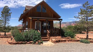 A wooden cabin with a porch, surrounded by red rock formations and sparse vegetation. - Torrey Pines Cozy Cabin! (Torrey)