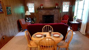 A dining area with a wooden table set for four, surrounded by wooden chairs. A red sofa is positioned against the wall, and a fireplace is visible in the background. - Welcome to Owls Nest Cabin NC!<br><br>Close to Wineries, waterfalls, antique shops etc (Otto)