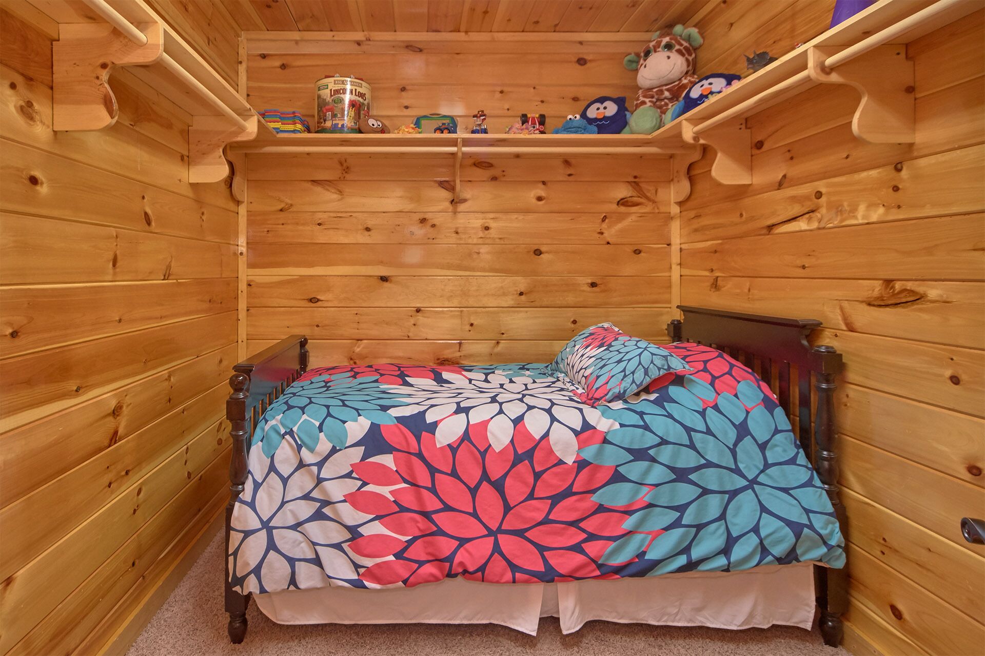 Una habitación tipo cabaña de madera con una cama, un estante con juguetes y una lata de Lincoln Logs.