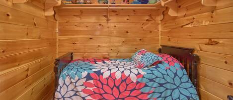 Una habitación tipo cabaña de madera con una cama, un estante con juguetes y una lata de Lincoln Logs.