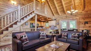A log cabin interior with a staircase, two leather sofas with patterned cushions, a wooden coffee table, and a kitchen area. - Black Bear Ridge - 5 Bedroom minutes from the Parkway! (Sevierville)