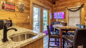 A wooden cabin interior with a kitchen area featuring granite countertops, a sink, and a dining table with leather chairs. - Black Bear Ridge - 5 Bedroom minutes from the Parkway! (Sevierville)